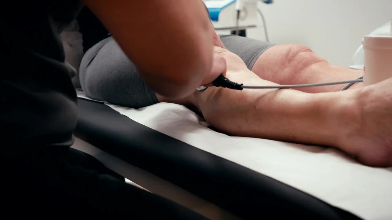 Mano de fisioterapeuta aplicando un cabezal con cable sobre la pierna de un paciente